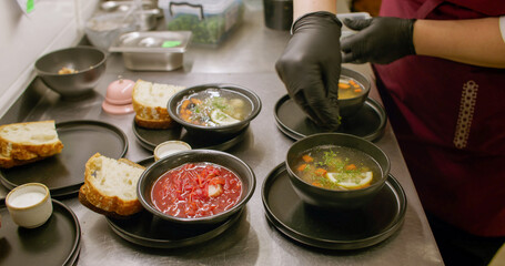 Serving meal. Kitchen process. Cafeteria chef garnishing hot dish with chopped fresh herbs. Hands adding aroma greens in soup borsch.