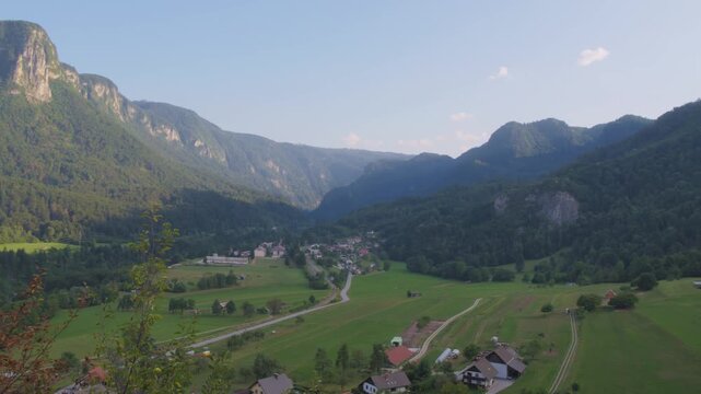 Left pan over Babji Zob valley above Bohinjska Bela, Slovenia, showing green fields, a winding road and forested peaks under soft afternoon light. Calm cinematic mood.
