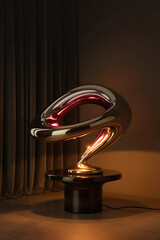 Modern sculptural lamp with a metallic finish, casting a warm glow on a dark background