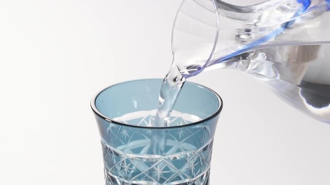 Pouring Sake into Traditional Japanese Kiriko Glass on White Background