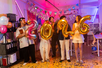 Asian business team celebrating New Year 2026 or major milestone achievement in office party,holding large 2026 foil number balloons and confetti falling.Concept of corporate success,festive teamwork 