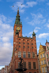 Gdansk clock tower stands tall over buildings and a fountain under blue sky