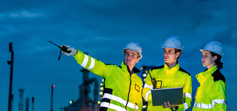 Petrochemical industry night engineer teamwork working on laptop Team of Petroleum in Glowing Workwear Collaborating oil refinery plant construction site at night