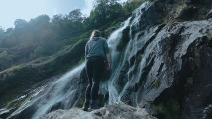 Woman admiring the powerful cascade of Powerscourt Waterfall. The immersive experience of nature in the heart of Ireland's Wicklow Mountains.