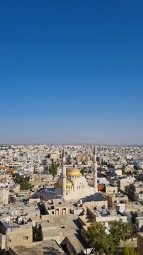 Vertical shot of Madaba, Jordan, with the King Hussein Mosque and its golden domes at the center, rooftops and streets stretching to the horizon on a sunny day under a blue sky