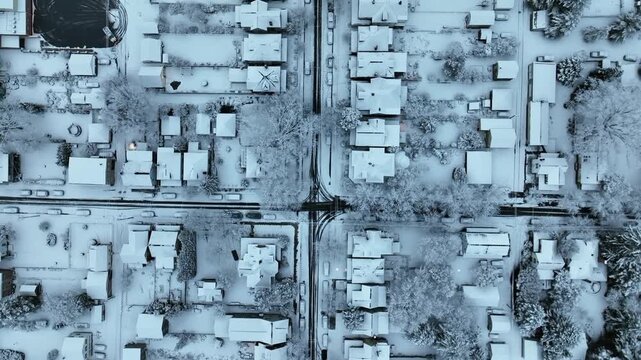 Top-down drone view of quiet American residential neighborhood after snowfall, with snow-covered houses, streets and trees. Row of houses with snowy roofs in quiet suburb.flyover.
