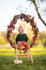 Lachendes Kleinkind sitzt auf Holzleiter in herbstlicher Natur mit K&uuml;rbissen und Bl&auml;tterkranz