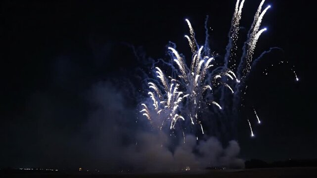 This video captures an impressive ground-level fireworks presentation, featuring brilliant blue and white light burst ascending into the dark night