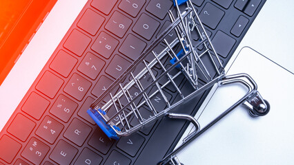 A shopping cart is on top of a laptop keyboard. The cart is silver and blue. The laptop is on a...