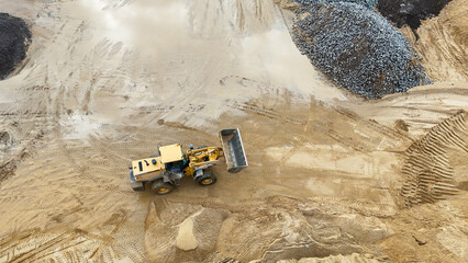 A large yellow bulldozer is driving through a muddy field. The dirt is wet and muddy, and the ground is uneven. The bulldozer is moving through the dirt, leaving a trail behind it