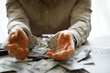 Hands of a fraudster with handcuffs on a background of us dollars. Fraud, cyber crime concept....