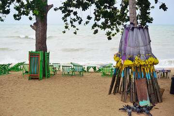 Beach chair and a group of umbrellas leaning against a tree