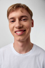 Closeup of a smiling young man in a white t shirt, casual style, bright expression, simple studio background, friendly and approachable image