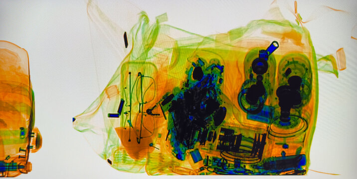 Colorful x ray image of luggage at security checkpoint showing electronics bottles and clothing, in bright green orange and blue tones ideal for travel safety and screening topics.