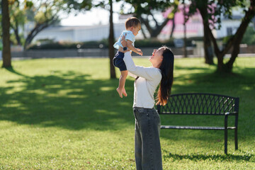 Mother lifting laughing baby boy in park