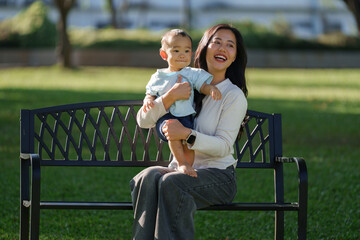 Happy asian mother holding baby enjoying park time