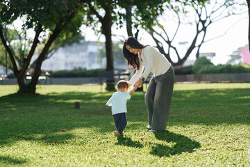 Mother helping toddler learning to walk in park