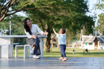 Mother encouraging child learning to walk outdoors at park