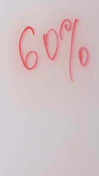 A hand holds a marker and writes percentages on a white background. The hand creates the numbers and percentage symbol using the marker. The writing indicates a sale.