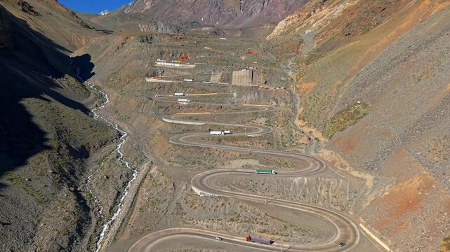 Aerial establishing view of Cuesta Caracoles hill with heavy trucks going up and down its curves on a sunny day
