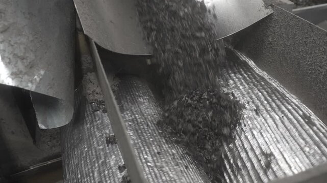 Shredded rubber disappears between rotating grooved metal rollers. Industrial recycling equipment performs compression and transfer stage