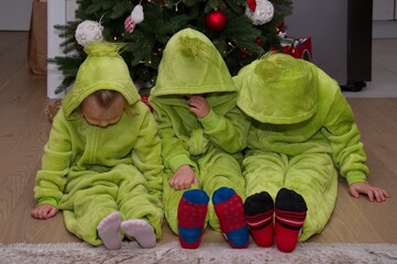 Cute little children dressed in a suitable costume sitting in front of Christmas tree