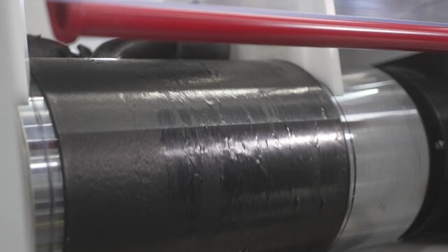 Man places wrinkled rubber onto rotating roller for surface smoothing. Industrial process shows material refinement for further processing