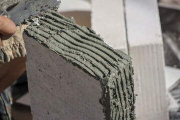 Worker applying thin adhesive mortar on aerated concrete block with notched trowel during wall construction, showing careful precision and focus on building steady foundation