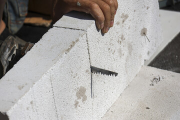 Close up construction worker hand diligently cutting lightweight concrete block using sharp manual...