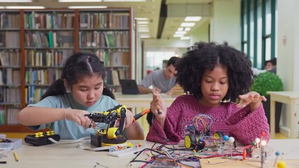 African American and Asian young girls study on robotic project in library.  - Powered by Adobe