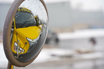 Almaty, Kazakhstan - 12.18.2025 : Reflection in the mirror. A yellow school bus in the parking lot. Winter time, snowfall.