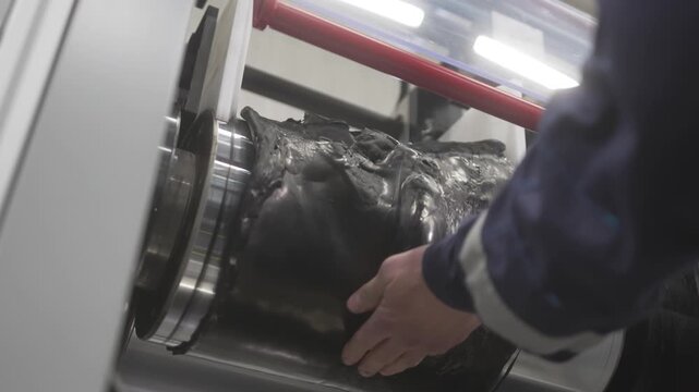 Worker processes recycled rubber mounted on rotating metal shaft. Rubber surface reshaping involves heat airflow and mechanical motion