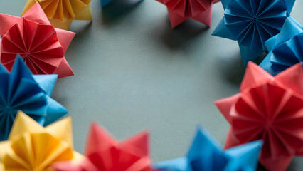 Colorful geometric origami stars circular frame, handmade folded paper craft border with copy space, macro close up art, for celebration, birthday, creative school project, background.