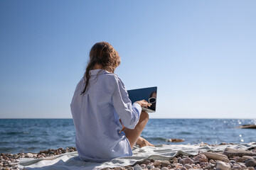 Laptop beach remote work person sits on pebble beach working by the calm sea clear blue sky copy space