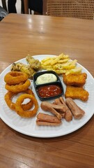 Diverse Platter of Golden Fried Snacks Featuring Crispy Fries, Onion Rings, Chicken Wings, and Fish Fingers with Sauces for Casual Dining