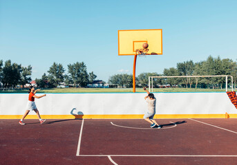 boy and girl play basketball on an empty outdoor court with copy space, concept of children sport, playground fitness, school promo