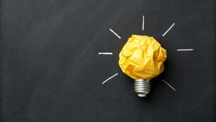 Light bulb made of crumpled yellow paper on blackboard background with chalk lines