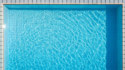 Clear water fills a swimming pool under bright sunlight in the afternoon hours with ripples on the surface