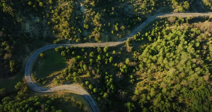 High and wide Top-down aerial of cyclists threading through the serpentine curves from Mirador de Fuebla to A&iacute;nsa highlands, framed by green canopy of UNESCO Sobrarbe-Pyrenees Geopark