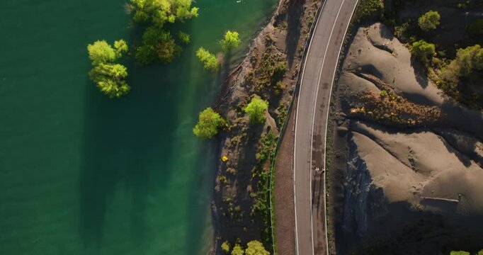 Top-down tracking shot of a cyclist navigating the ruins of the Antiguo Balneario de Tiermas along the turquoise shores of the Yesa Reservoir in Zaragoza, Spain.