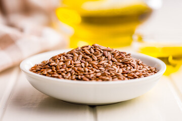 Brown linseed or flaxseed and oil. Healthy flax seed in bowl on white table.