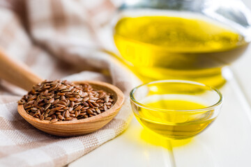 Brown linseed or flaxseed and oil. Healthy flax seed on wooden spoon on white table.