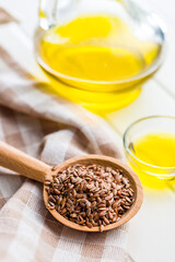 Brown linseed or flaxseed and oil. Healthy flax seed on wooden spoon on white table.