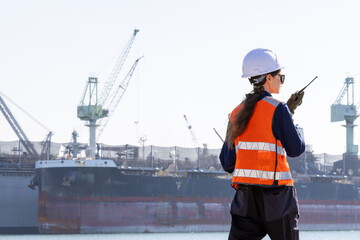 group of industrial engineers workers in a refinery - oil and gas processing equipment and machinery, engineers collaborate with a laptop, blueprint, and digital tablet at the oil storage tanks site.