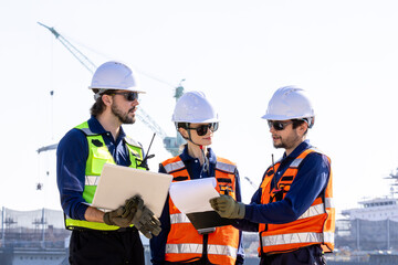 group of industrial engineers workers in a refinery - oil and gas processing equipment and machinery, engineers collaborate with a laptop, blueprint, and digital tablet at the oil storage tanks site.