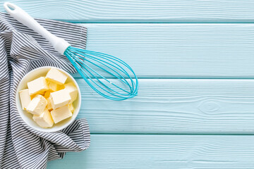 Butter sliced in white bowl with napkin and a whisk, top view