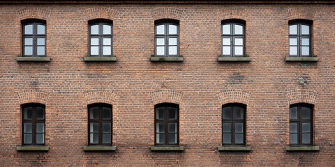 Fototapeta premium Old red brick industrial building facade showing arched windows and textured wall background