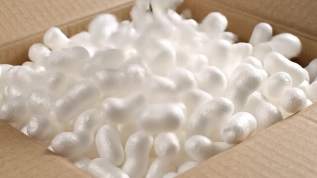 White Styrofoam packing peanuts falling into a cardboard box to fill it up close up