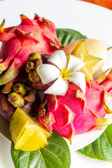 Plate full of different tropical fruits. Healthy vegetarian food. Pitaya fruit, lychee, mangosteen on white table.