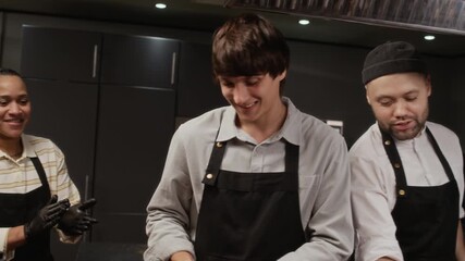 Male culinary course trainee scooping chocolate dough into cupcake mold using ladle in group class then groupmates congratulating student with applause in restaurant kitchen